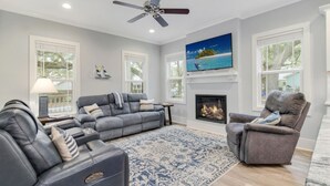 A modern living room with a fireplace, a large TV mounted above it, and a ceiling fan.