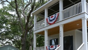 A two-story building with a porch, steps, and a flag.