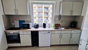 Une cuisine compacte équipée d’un lave-vaisselle, d’un four et d’une fenêtre donnant sur un immeuble d’habitation.