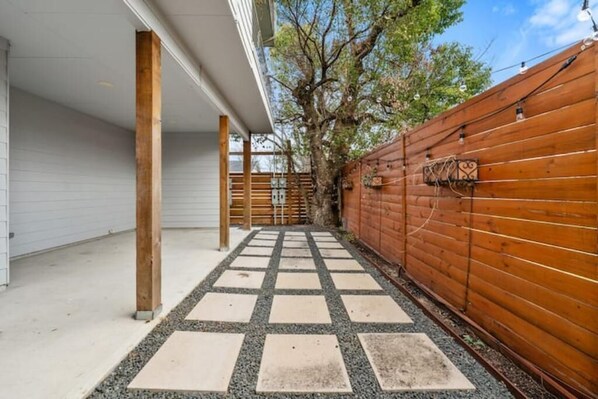 Un espacio al aire libre cubierto con cerca de madera, un camino de baldosas y un árbol.