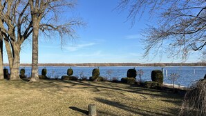 A lakeside view with a grassy area, a wooden fence, and several trees.