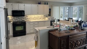 A modern kitchen with white cabinets, a black oven, a microwave, and a large window providing a view of trees.