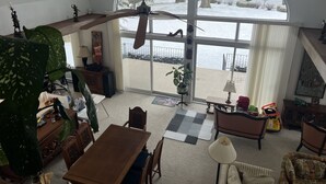 A spacious living room with a large window overlooking a snowy landscape, a ceiling fan, and a variety of furniture including a wooden dining table and chairs.
