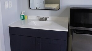 Un bagno con un lavandino bianco, mobili scuri blu, uno specchio grande e un forno a microonde integrato.