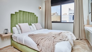 Un dormitorio moderno con cabecera verde, un ventanal con cortinas y vistas a edificios.