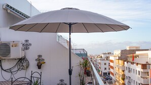 Un balcón con mesa, sillas, una sombrilla y plantas en macetas.