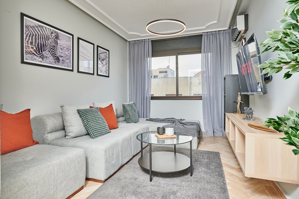 A modern living room with a grey sofa, a round coffee table, and a TV mounted on the wall.