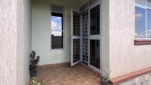 Un espace extérieur abrité, doté d’un sol carrelé, de plantes en pot et d’un ensemble de portes vitrées donnant sur un espace intérieur.