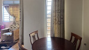 Un coin repas avec une table ronde et des chaises, un canapé en osier agrémenté de coussins à motifs et une fenêtre avec des rideaux.