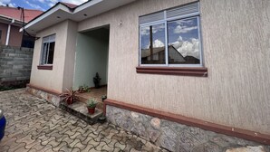 Une maison à deux étages avec une terrasse carrelée, un petit jardin agrémenté de plantes en pot et une cheminée bien visible.