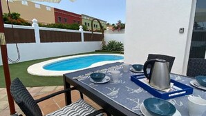 A patio with a pool, outdoor furniture, and a table set for dining.