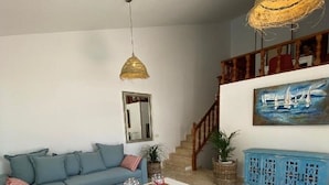 A living room with a blue sofa, a white coffee table, a woven rug, a painting of sailboats, and a staircase.