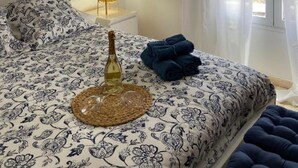 A bedroom with a bed, a bedside lamp, a painting, and a window with curtains.
