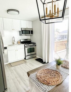 A modern kitchen with white cabinets, a microwave, stove, and a hanging light fixture. - Family Retreat-Walk to Lake-Cedar Point-Deck/Grill (Vermilion)