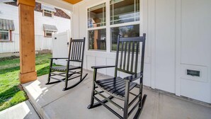 A porch with two rocking chairs, a wooden ceiling, and a white exterior wall with windows.