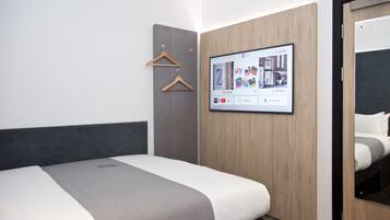 A modern hotel room with a bed, a wardrobe, and a mounted TV displaying the hotel's website.