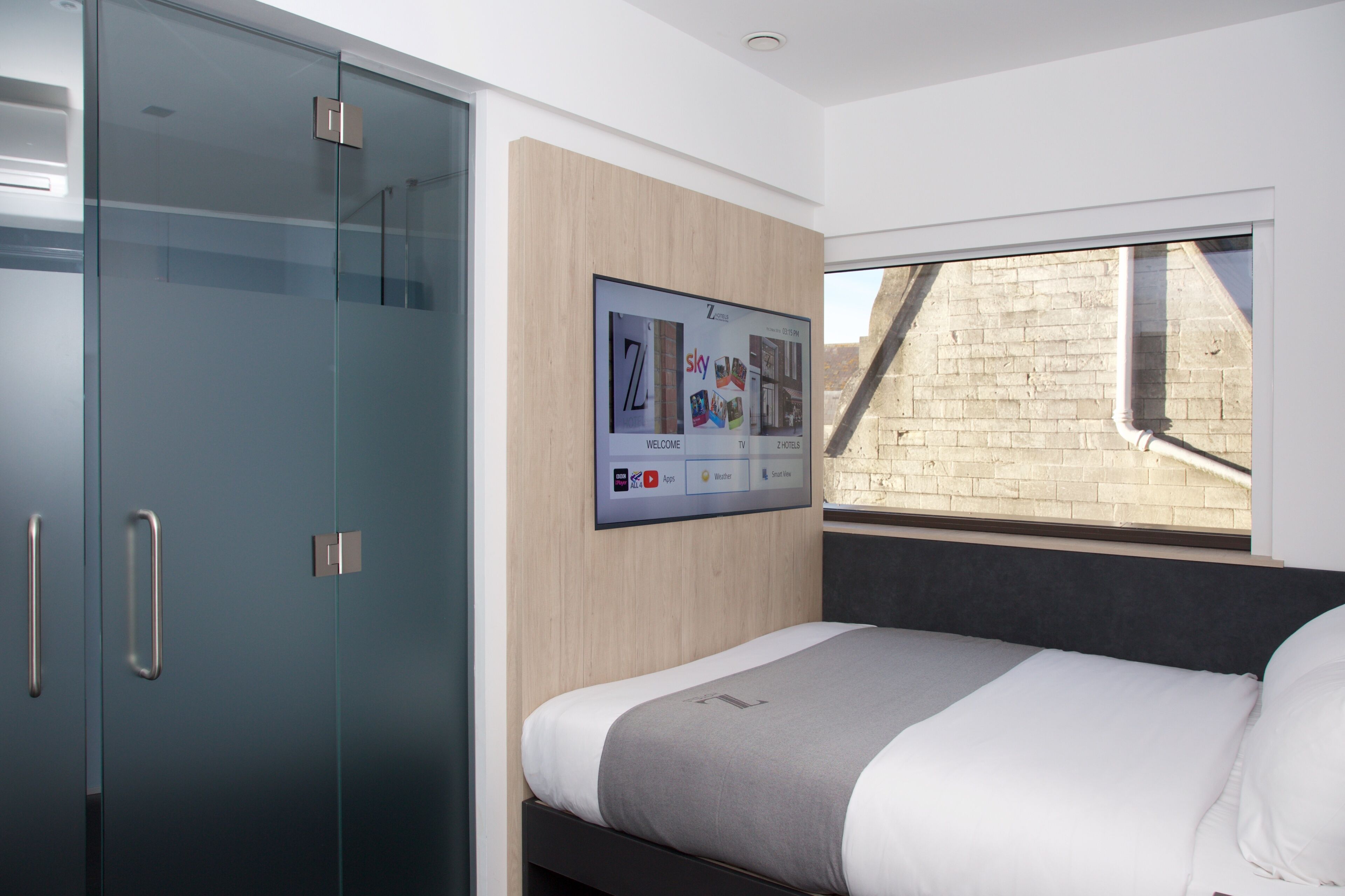 A modern bedroom with a bed, a wardrobe, and a digital display on the wall.