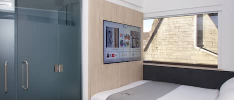 A modern bedroom with a bed, a wardrobe, and a digital display on the wall.