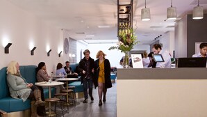Un hall d’hôtel moderne, doté d’espaces aménagés avec des sièges, d’un comptoir de réception et d’une horloge bien visible au mur.