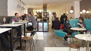 Un restaurant moderne avec des tables hautes et des tabourets, un coin bar et différents types de sièges, notamment un canapé turquoise et une table ronde.