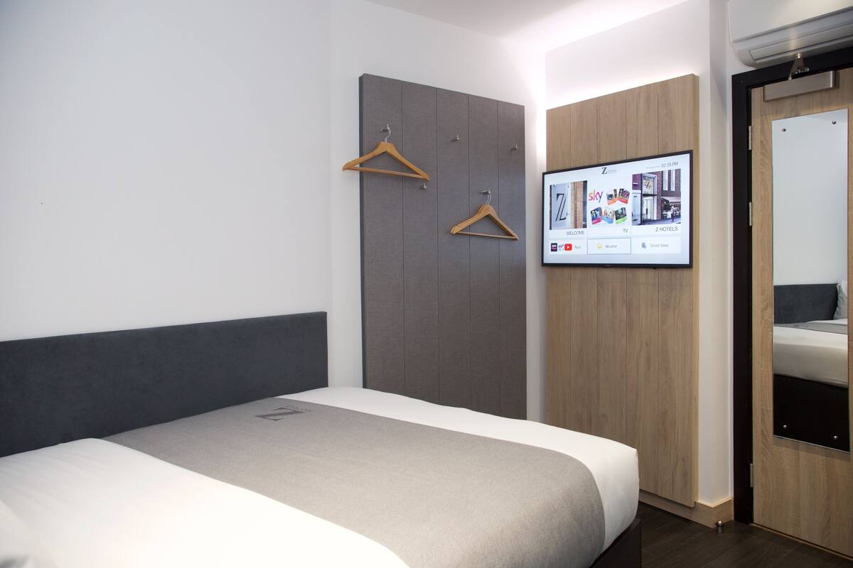 A modern hotel room with a large bed, a wardrobe, and a mounted TV displaying a welcome screen.