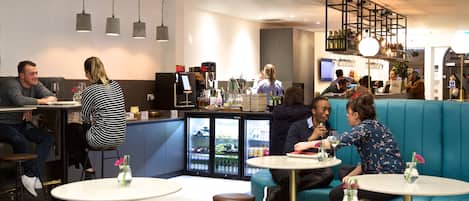 Un café moderno con mesas redondas, asientos en la barra y una zona de mostrador.