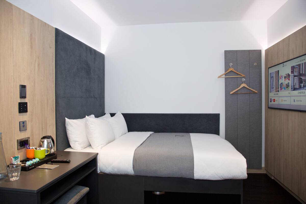 A modern hotel room with a large bed, a desk with a coffee maker, and a TV mounted on the wall.