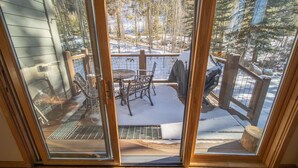 A view through a glass door of a wooden deck with a metal table and chairs, surrounded by snow and trees. - Northstar 1961 (Keystone)