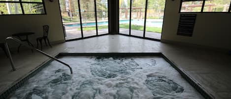 A spa area with a hot tub, large windows, and a view of a pool and garden.