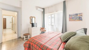 Un dormitori amb un llit, una cadira, una petjarrera, un televisor i un quadre a la paret.