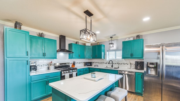 Una cocina moderna con armarios color turquesa, un refrigerador de acero inoxidable y una isla central con taburetes de bar.