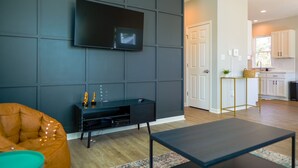 Ein modernes Wohnzimmer mit einem Flachbildfernseher an einer dunklen Wand, einem bequemen orangefarbenen Sofa und einem schlichten Couchtisch.