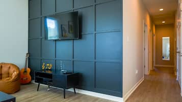 Una sala de estar moderna con una pared de acento oscura, un televisor montado, un sillón de cuero y una guitarra.