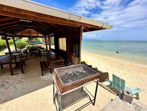 A beachside restaurant with outdoor seating, a grill, and a view of the ocean.