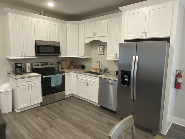 A modern kitchen with white cabinets, stainless steel appliances, a microwave, oven, dishwasher, and a refrigerator.