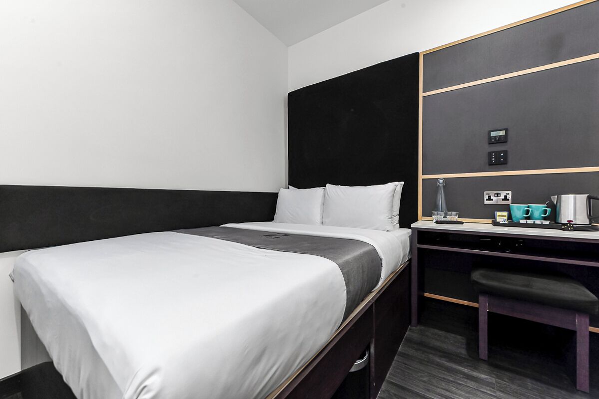 A hotel room with a bed, a desk, a chair, and a mirror.