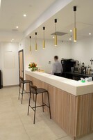 A modern bar area with a counter, bar stools, pendant lighting, and a coffee machine.