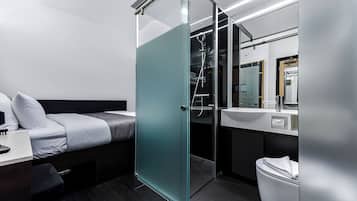 Ein modernes Hotelzimmer mit Bett, Glasdusche, Waschbecken und Toilette.