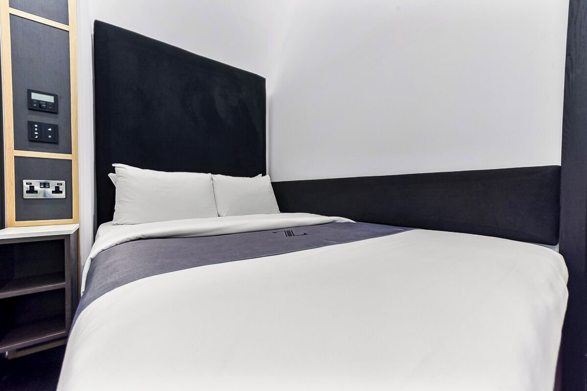A modern hotel room with a large bed, a control panel, and a built-in shelf.