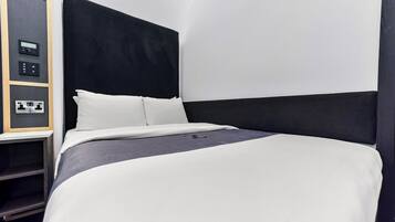 A modern hotel room with a large bed, a control panel, and a built-in shelf.