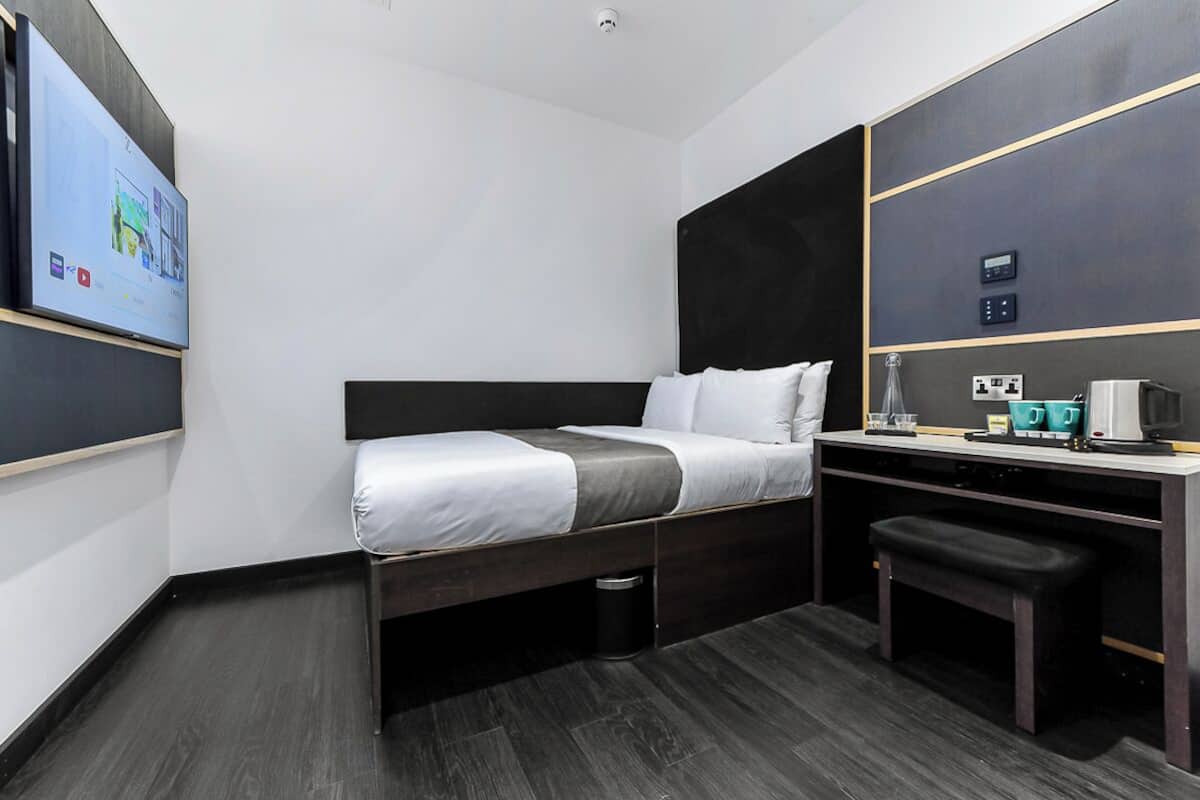 Moderni hotellihuone, jossa on sänky, työpöytä, tuoli, televisio ja kahvinkeitin.