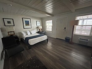 A bedroom with a bed, bedside tables, a lamp, framed pictures, a door, and a window with blinds. - STERLING GARDENS HOTEL (Las Vegas)