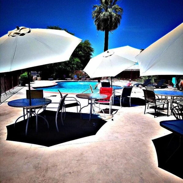 A poolside area with umbrellas, lounge chairs, and a pool. - STERLING GARDENS HOTEL (Las Vegas)