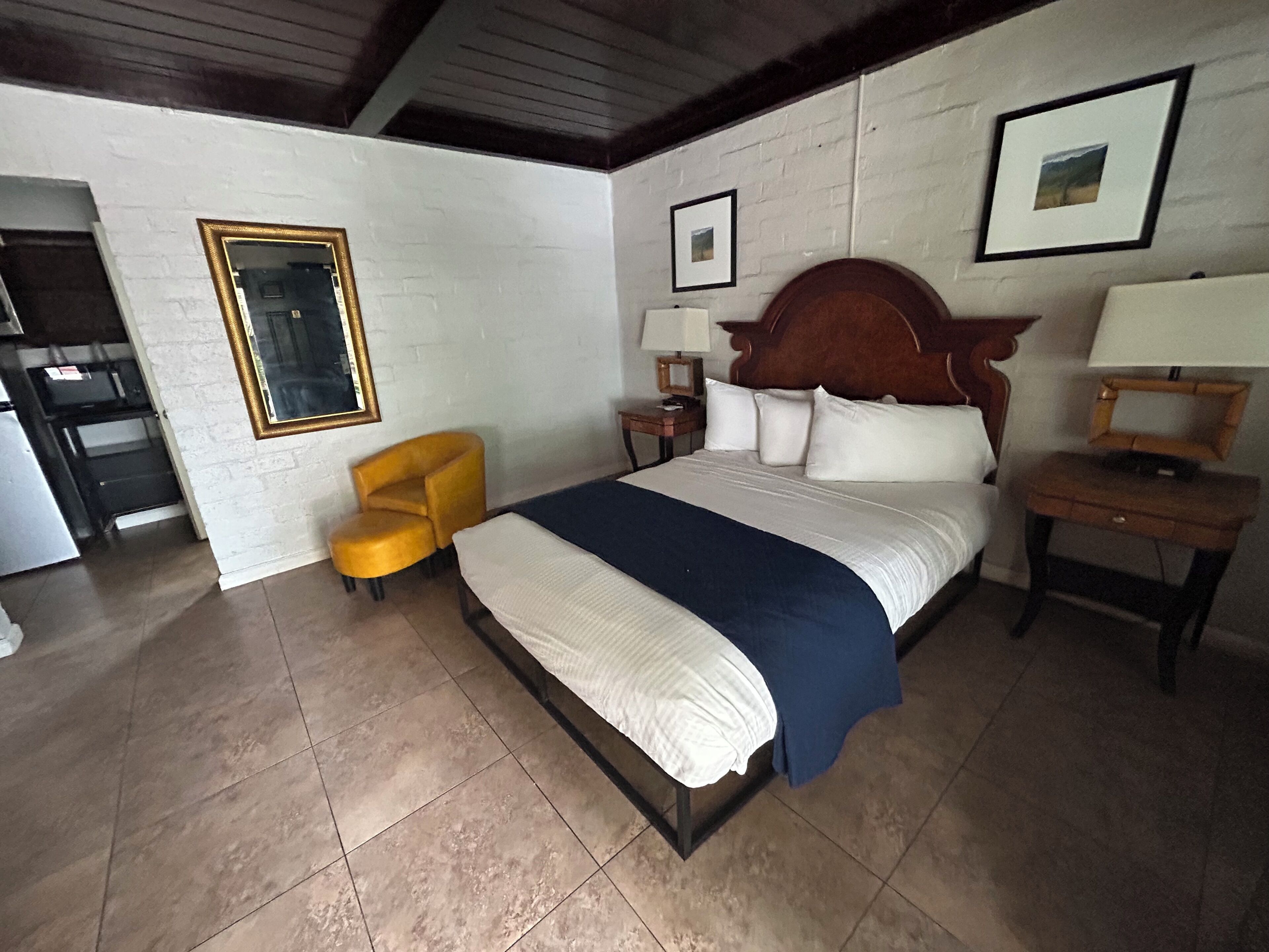 A hotel room with a bed, a chair, a nightstand, a lamp, and a picture on the wall.