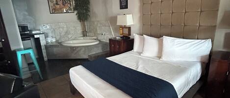 Une chambre d’hôtel comprenant un lit, une table de chevet, une lampe, un téléviseur fixé au mur, une salle de bain avec baignoire et un plafond décoré avec un motif de ciel peint.