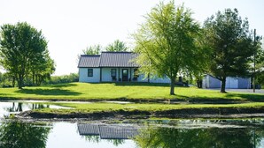 A modern house with a sloped roof, a front porch, and a small pond in the foreground. - The Pond View House - quiet country getaway w/ hot tub
 (Leesburg)