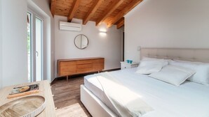 Quarto com teto de madeira, cama com roupa de cama branca, cômoda de madeira e espelho redondo na parede.
