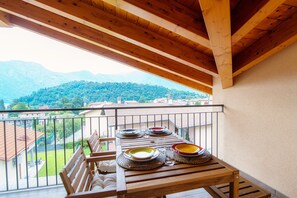 A wooden balcony with a table set for dining, overlooking a mountainous landscape. - Serendipity (Tremezzina)