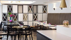 A modern restaurant interior with a central seating area, a decorative wall with wine racks, and a bar counter. - Z Tottenham Court Road (London)