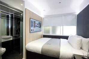 Une chambre d’hôtel moderne équipée d’un lit, d’un téléviseur fixé au mur, d’une douche en verre et d’une grande fenêtre.